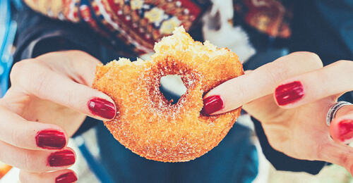 Bilde av hender som holder en halvspist donut med sukker på