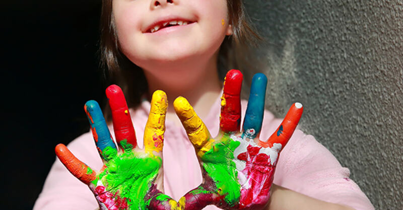 Bilde av en glad jente som holder sine åpne malte hender opp foran seg
