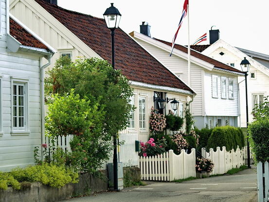 Bygate hvit bygg med trær og hekker foran