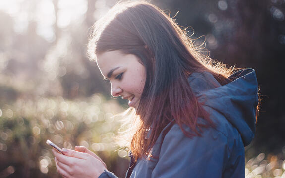 En ung jente holder en mobil i hånda og smiler mot skjermen. Foto