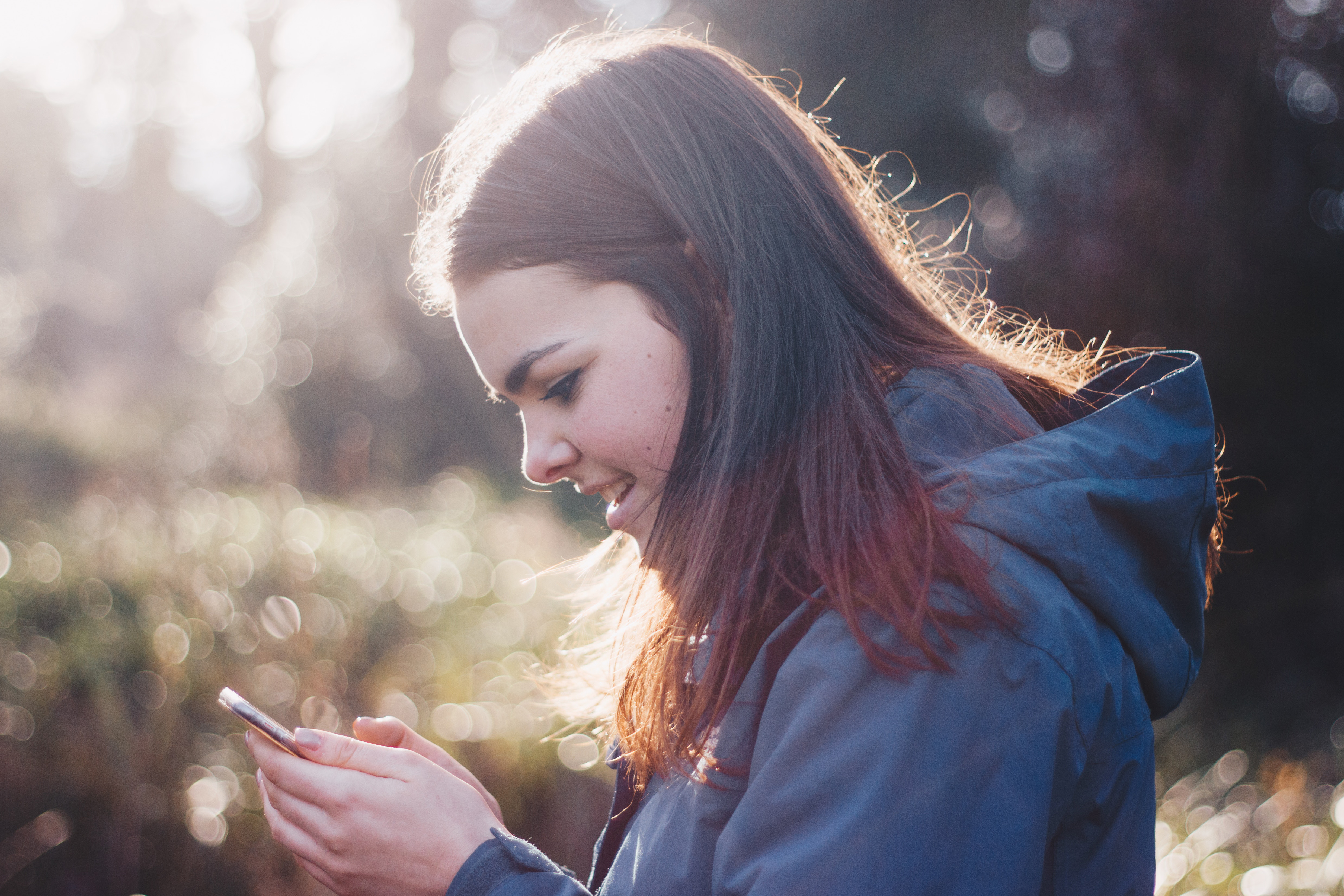 En ung jente holder en mobil i hånda og smiler mot skjermen. Foto