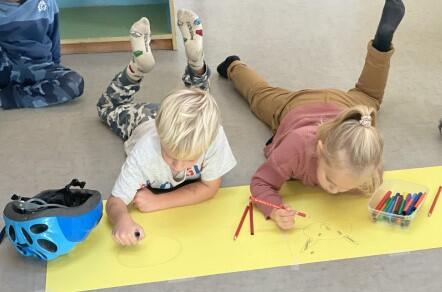 To barn ligg på magen på gulvet og teiknar