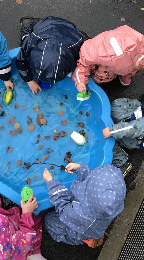 bildet viser barn som leker med lekebåter i en balje fylt med vann