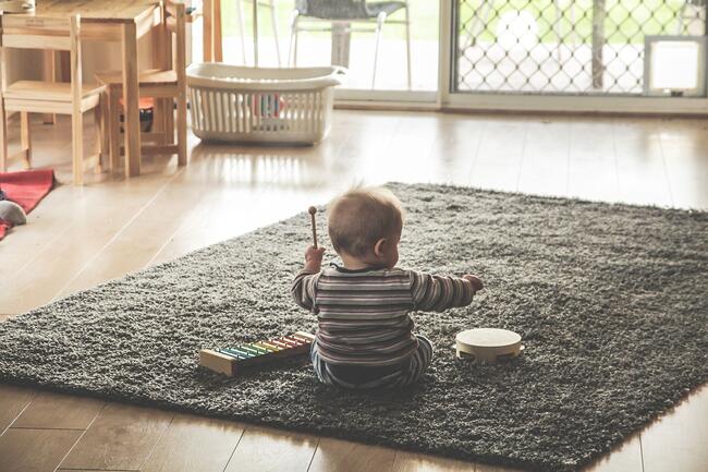 lite barn sit på eit teppe og spelar på tromme