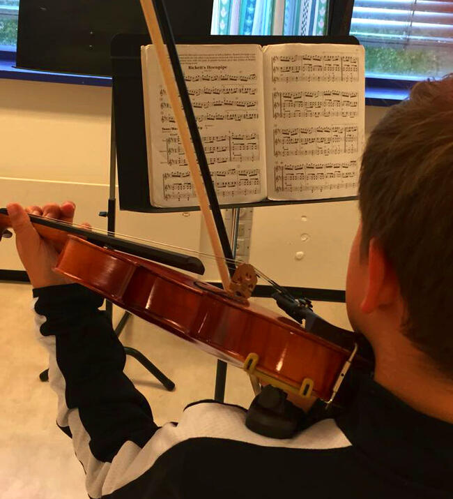 gut spelar fiolin med notar på notestativ forran seg