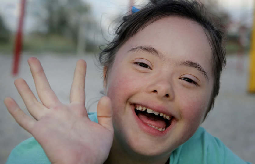 Foto som viser en glad jente med Downs syndrom som holder hånden opp til hilsen