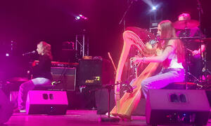 To jenter på scene. En spiller piano og synger, den andre spiler harpe og synger