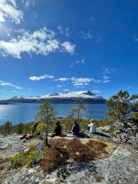 Fem mennesker sitter på fjelltopp med fin utsikt