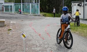 En gutt i hvitt t-skjorte og blå sykkelhjelmen sykler på skolegård
