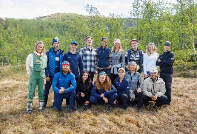 Gruppe av 15 mennesker i turklær står i skogen