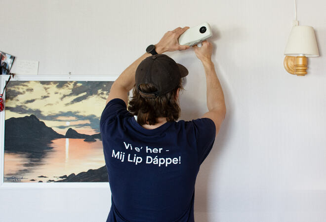 Ansatte i Hamarøy kommune i blå t-skjorte monterer hvill boks på veggen