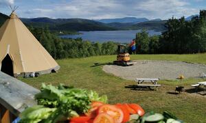 Stor lavvo står på marka, innsjø i nærheten, tallerken med salat står på veranda