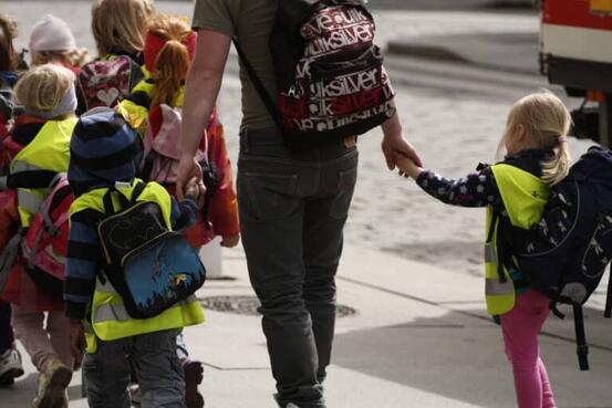 bilde av barn med sekk som holder en voksen i handa