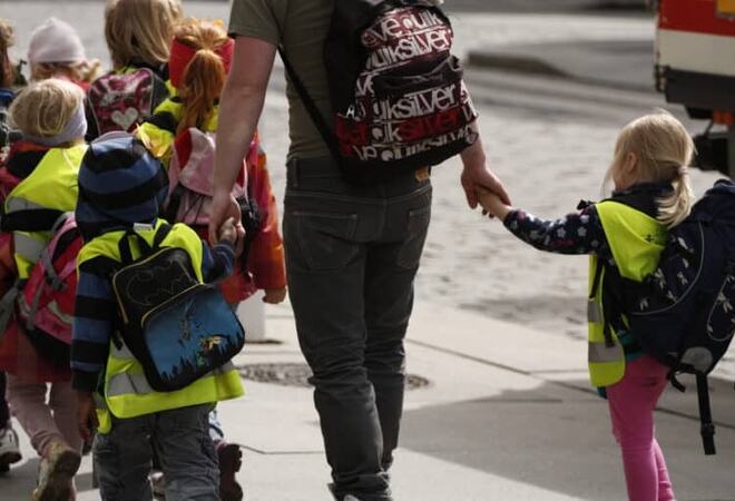 bilde av barn med sekk som holder en voksen i handa