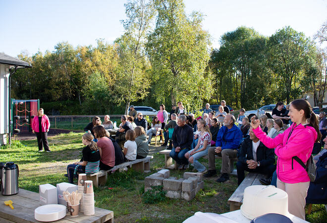 Masse folk sitter og står ute ved barnehage i fin solvær