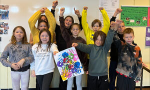 Gruppe av glade barn står i klasserommet, to hålder plakat med logo Vi e her