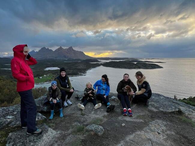 5 voksne, 2 barn og 1 hund på fjelltoppen med utsikt mot hvet