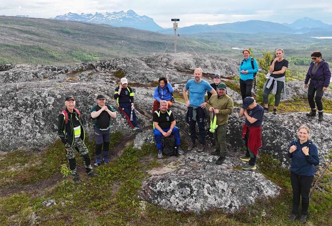 12 mennesker i turklær står på toppen av fjell