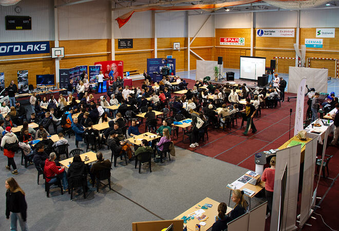 Masse bord i Hamarøyhallen med ungdom og vokne, scene i midten