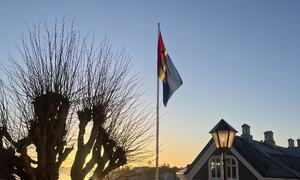 Bildet viser det samiske flagget heist utenfor husan med soloppgangen i bakgrunn