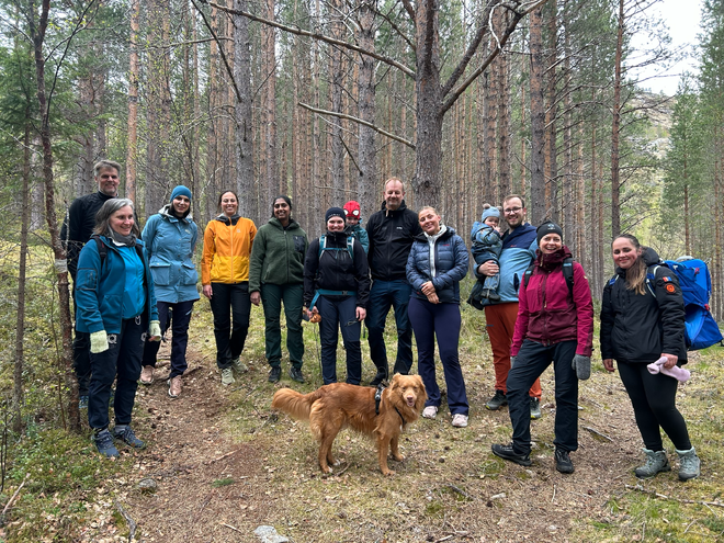 Masse folk i turklær med barn og hund står i skogen