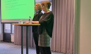 To damer har foredrag ved stor skjermen