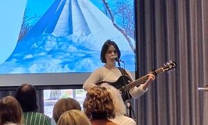 En kvinne spiller gitar og synger, flere hører
