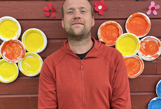En mann i rød sjorte sitter ved veggen med store blomster på
