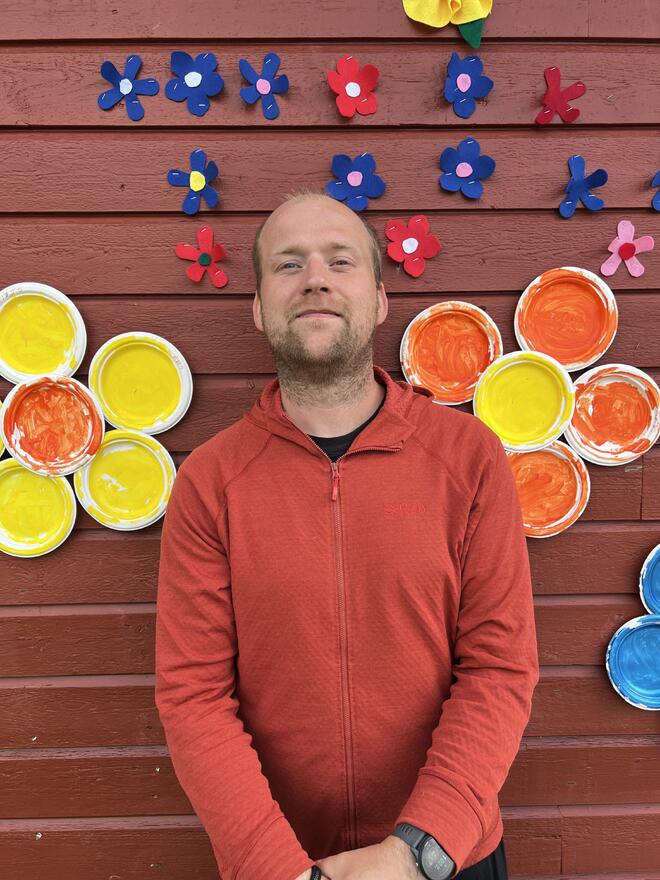 En mann i rød sjorte sitter ved veggen med store blomster på