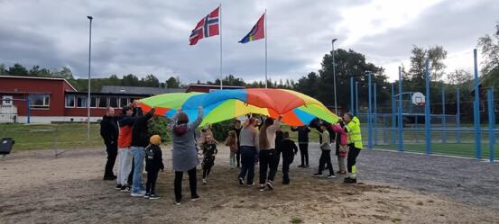 Masse barn og voksen står i sirkel og holder rengbue seil
