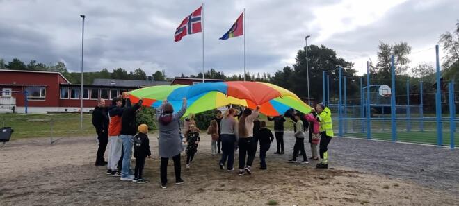 Masse barn og voksen står i sirkel og holder rengbue seil