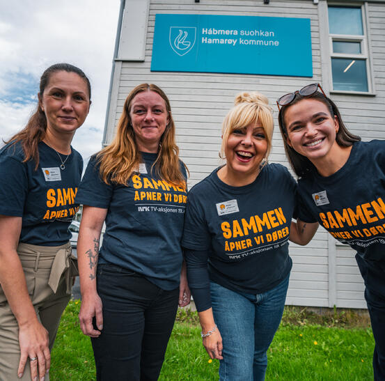 Fire kviner står og smiler, logo til Hamarøy kommune bak på veggen