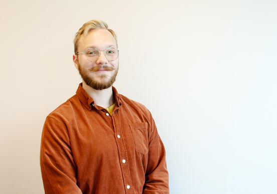En mann med bart i briller i oransje sjorte