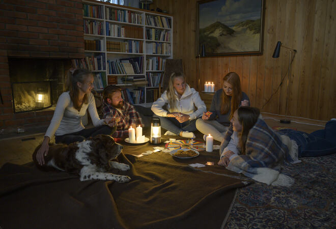 Strømbrudd Strømbrudd. Fem unge mennesker sitter i stua foran peisen med pledd rundt seg og spiller spill.