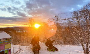 Barn leker ute i sne mned sol i bakgrunn
