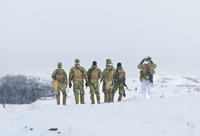 6 seks soldater står ute i feltet og speider mot horisonten. De er markører i felt.