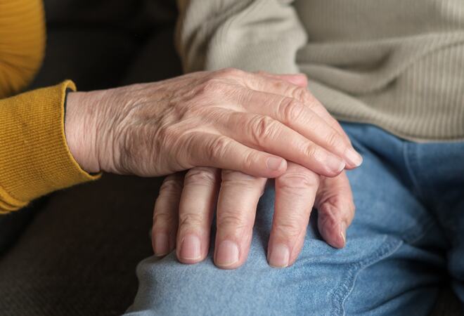 To personer sitter ved siden av hverandre. Den ene har lagt hånden på den andres hånd